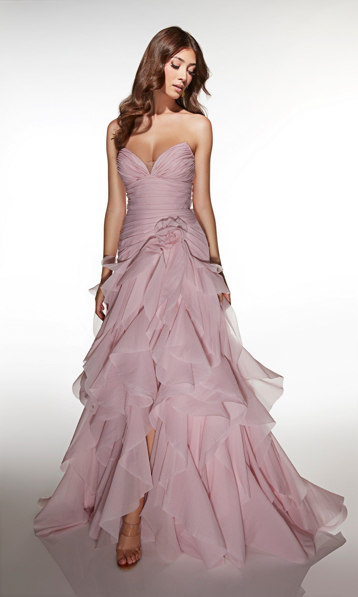 A woman wearing the Alyce 62024 long prom dress—a strapless, light pink, floor-length ruffled gown—stands against a plain white background.